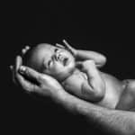 Schwarzweiß Bild von einem Babyshooting mit den Händen des Vaters. Die ersten Familienfotos.