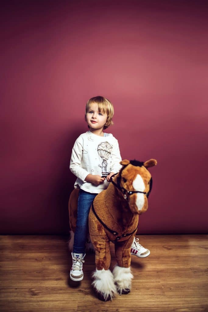 Kind sitzt beim Kinderfotoshooting auf ihrem grossen Kuscheltierpferd.
